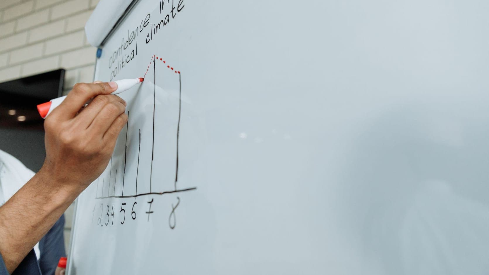 A person writing bullet points on a large whiteboard in a bright room.