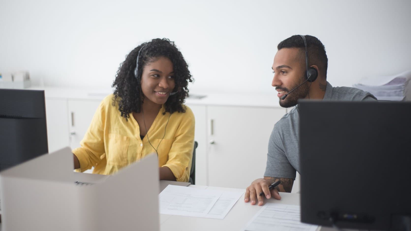 Two sales representatives on headsets rehearsing a sales pitch together